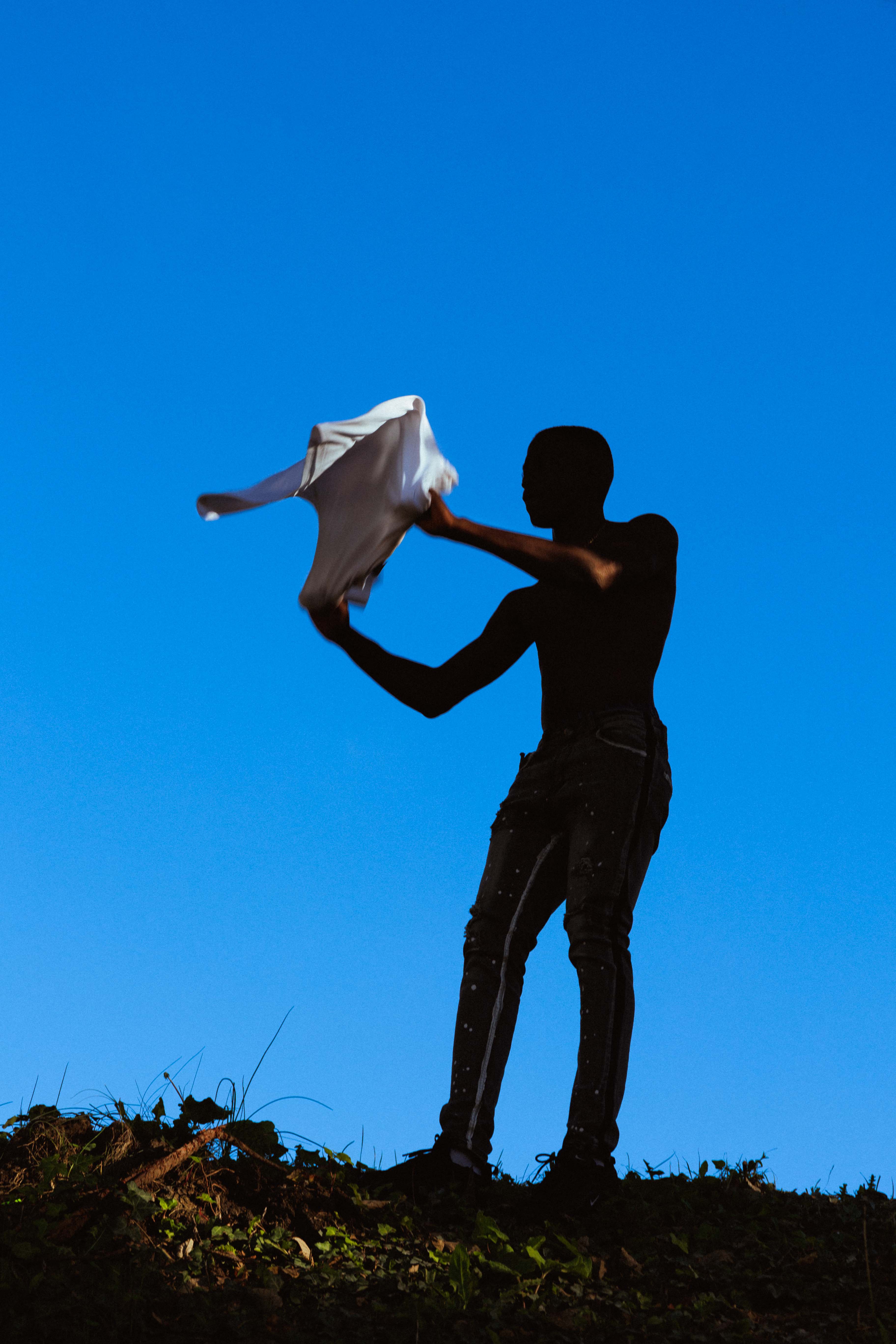 Photograph of a almost silhouetted figure against a blue field with fabric between their hands